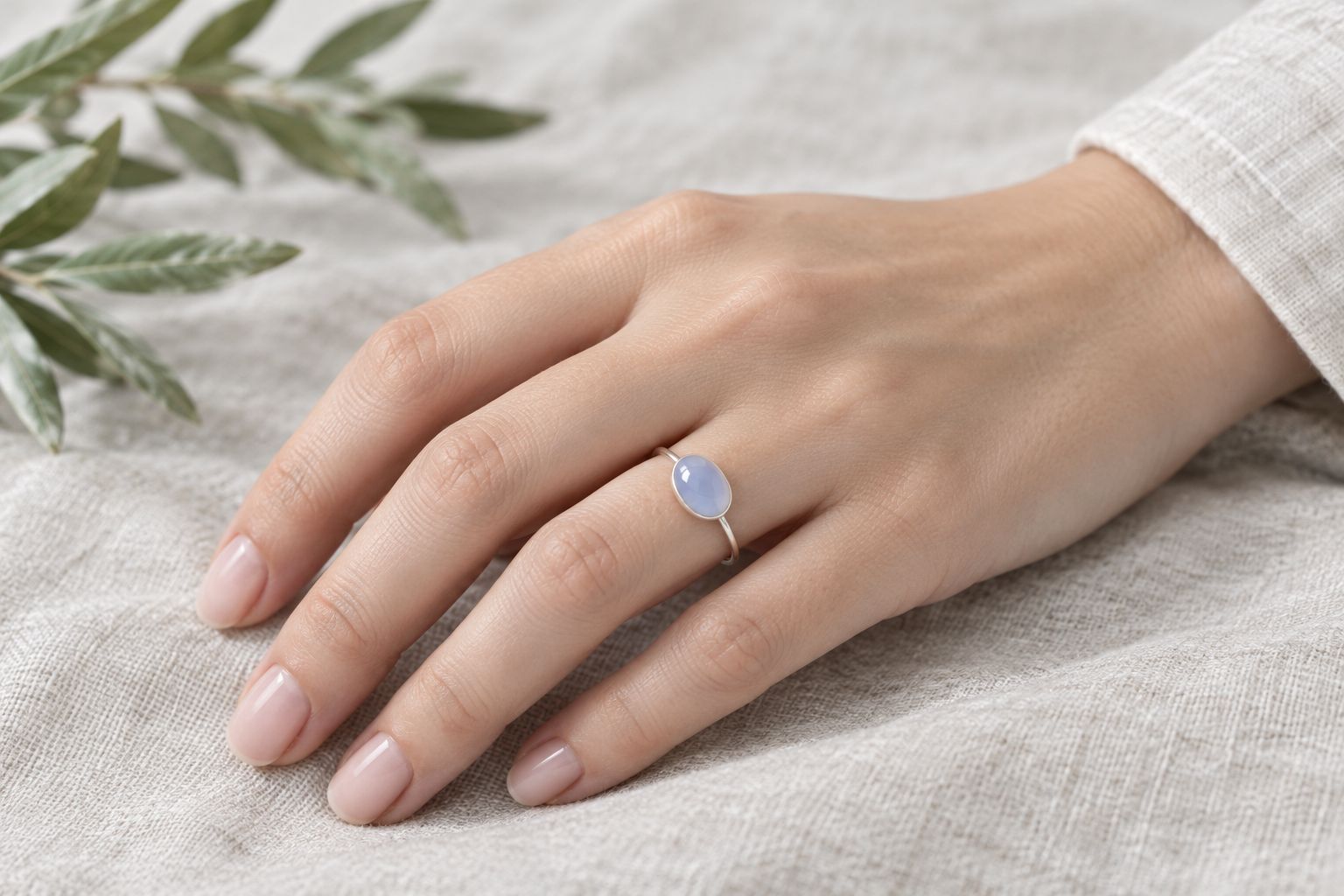 Hand wearing a thin silver ring set with a pale blue cabochon stone