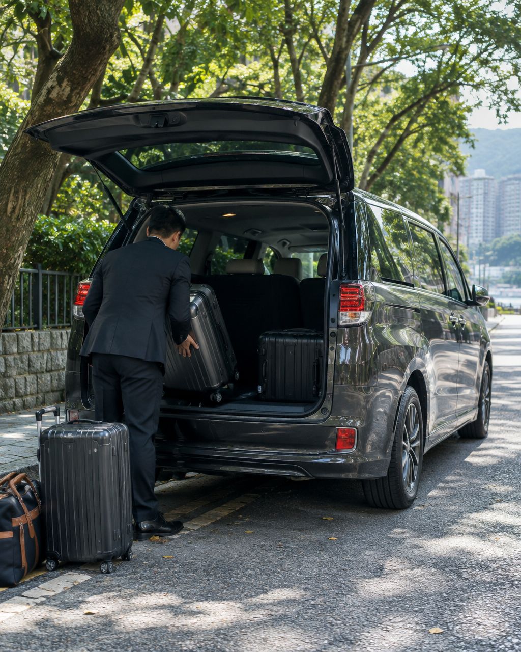 A Mayline chauffeur loading suitcases into the boot of a dark grey MPV on a leafy street near The Royal Garden in Tsim Sha Tsui East