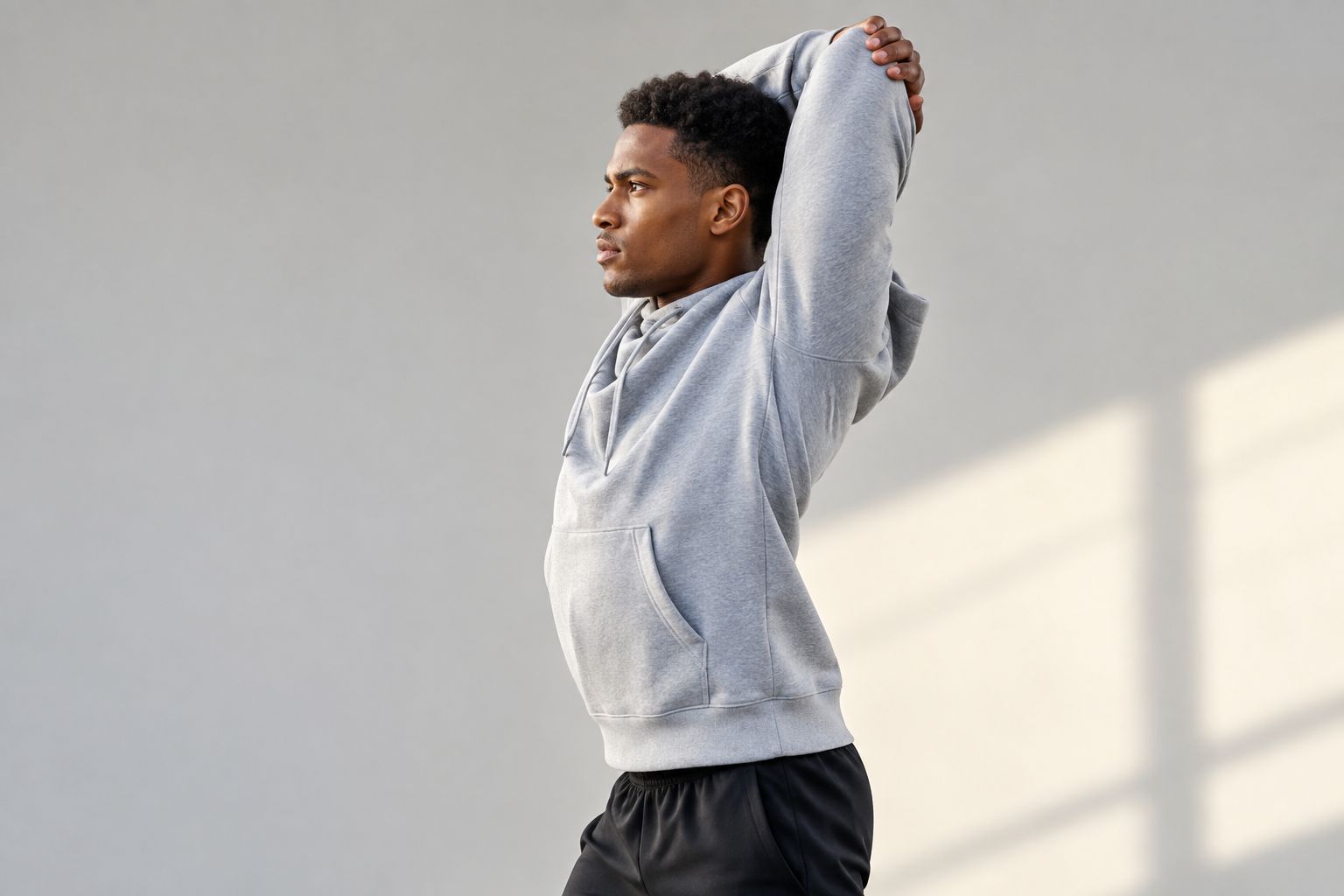 Athlete checking hoodie shoulder and hem fit during an overhead reach