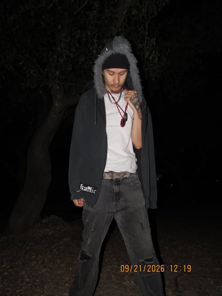 Person outdoors at night wearing a fur-trimmed dark hood, white shirt and dark jeans, with a yellow camera timestamp.