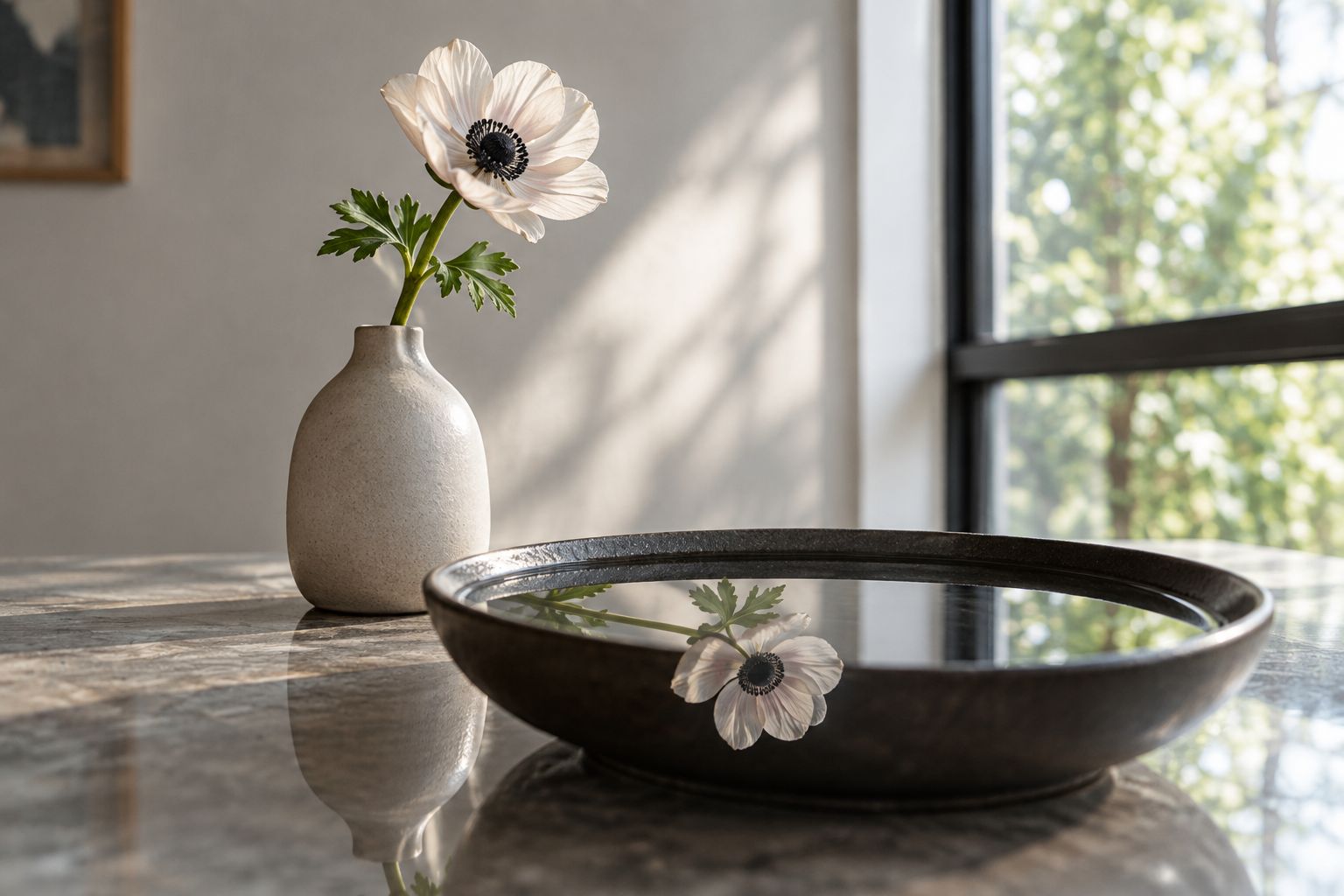 A flower beside a shallow dish, with its reflection visible in still water