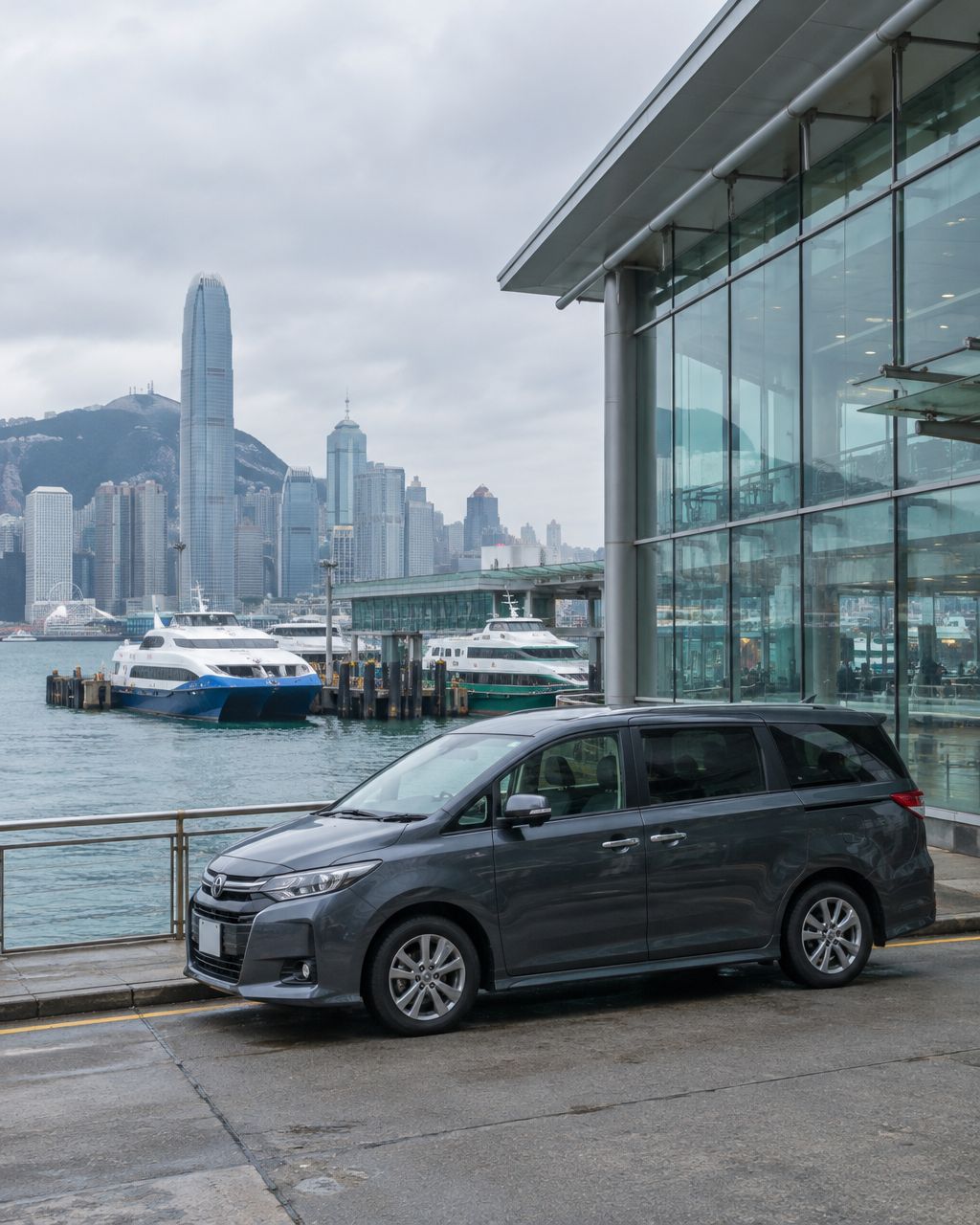 A dark grey Mayline MPV waiting beside the glass China Ferry Terminal building on the Hong Kong waterfront