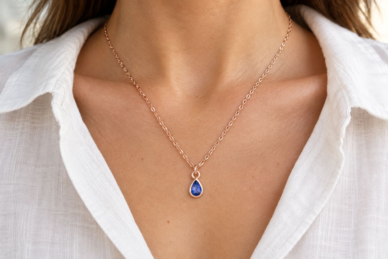 A pear-cut birthstone necklace worn against an open linen neckline