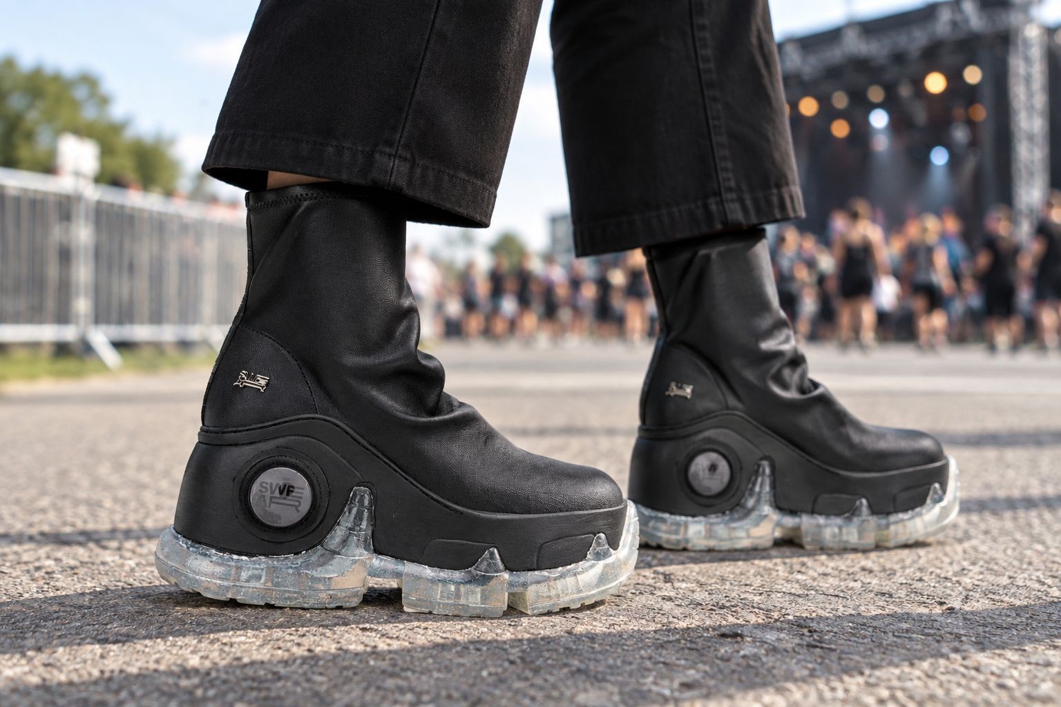 Black platform boots worn with cropped trousers on a dry concert walkway