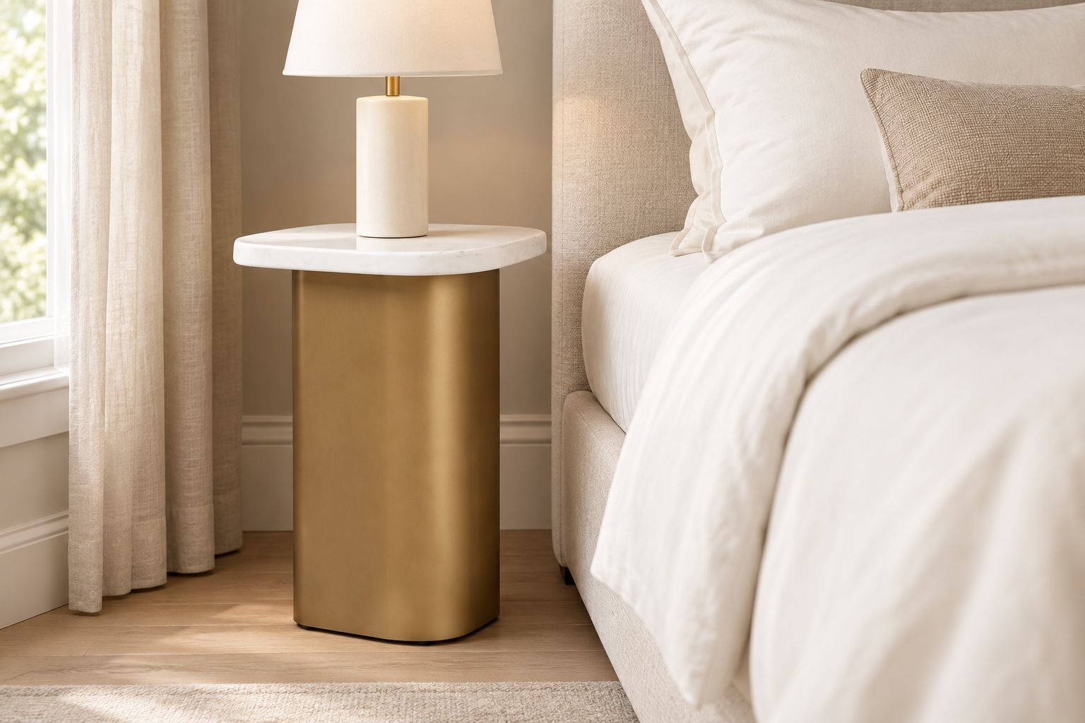 White marble and antique gold side table beside an upholstered bed with ivory bedding
