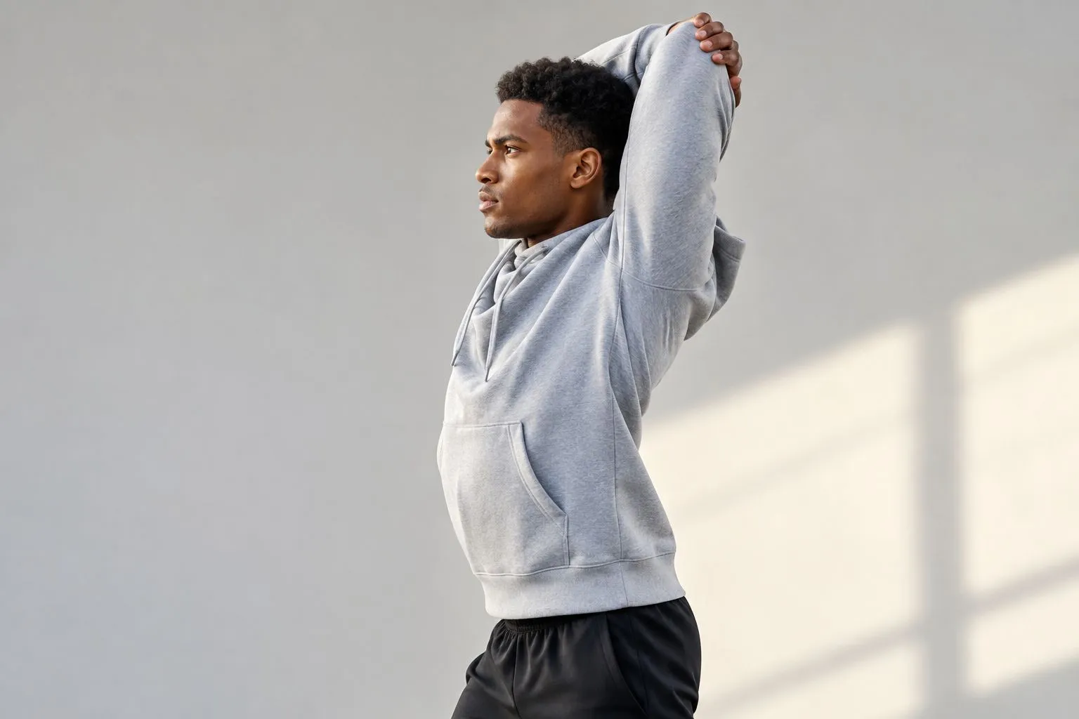 Athlete checking hoodie shoulder and hem fit during an overhead reach